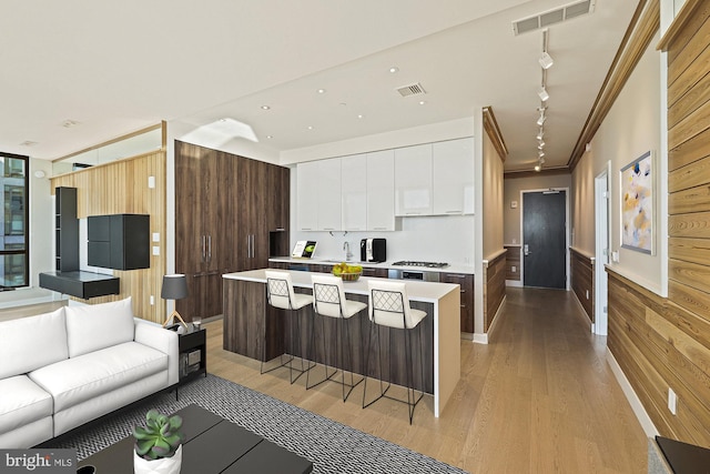 kitchen with a breakfast bar, a center island, wood walls, white cabinets, and light wood-type flooring