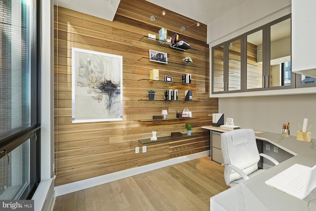 office area featuring wooden walls, built in desk, and light hardwood / wood-style flooring