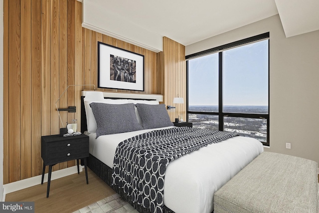 bedroom featuring multiple windows, light wood-type flooring, and wood walls