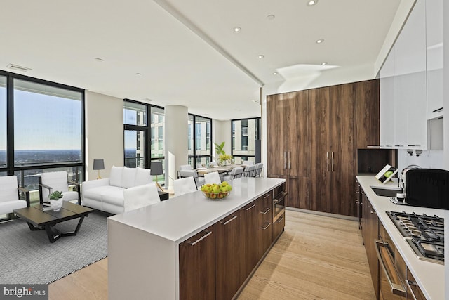 kitchen featuring floor to ceiling windows, a center island, stainless steel gas stovetop, light hardwood / wood-style floors, and white cabinets