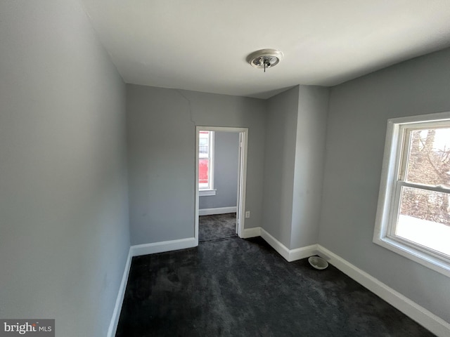 empty room featuring dark colored carpet and a wealth of natural light