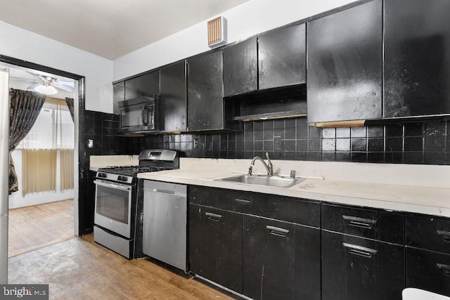 kitchen featuring appliances with stainless steel finishes, tasteful backsplash, sink, light hardwood / wood-style flooring, and ceiling fan