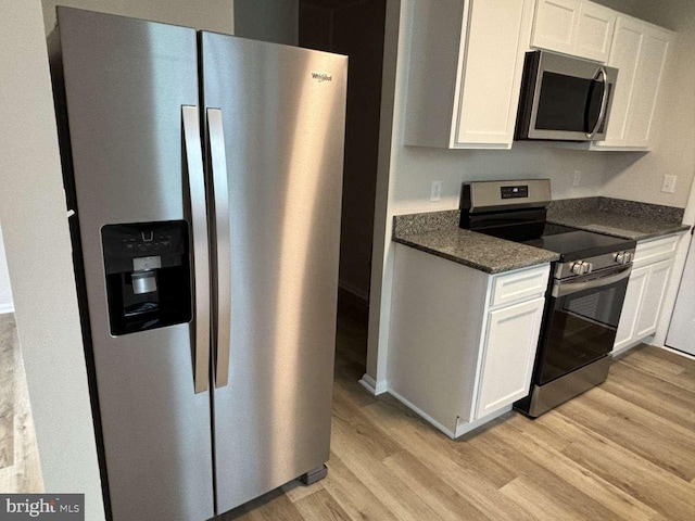 kitchen with stainless steel appliances, white cabinetry, dark stone counters, and light hardwood / wood-style flooring