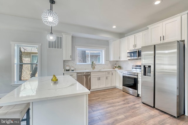 kitchen featuring stainless steel appliances, light stone countertops, white cabinets, and decorative light fixtures