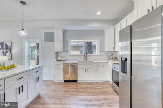 kitchen featuring white cabinetry, appliances with stainless steel finishes, decorative light fixtures, and light stone countertops