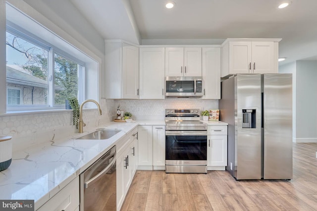 kitchen featuring sink, white cabinetry, light stone counters, appliances with stainless steel finishes, and light hardwood / wood-style floors