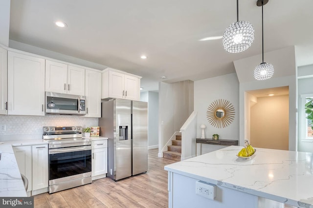 kitchen featuring white cabinetry, hanging light fixtures, light wood-type flooring, and appliances with stainless steel finishes