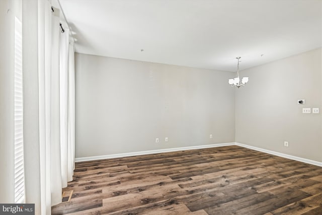 unfurnished room featuring dark wood-type flooring and a notable chandelier