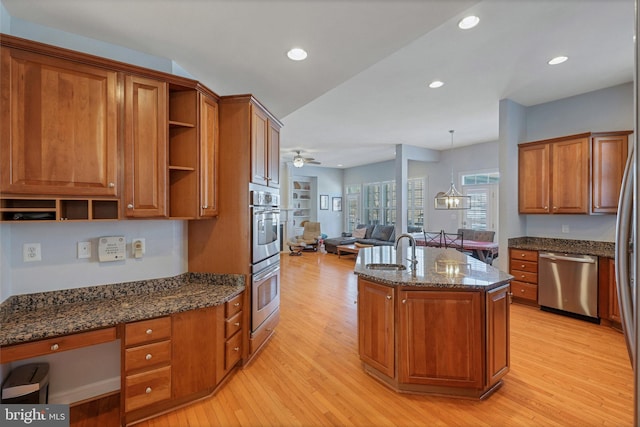 kitchen featuring stainless steel appliances, an island with sink, decorative light fixtures, and dark stone counters