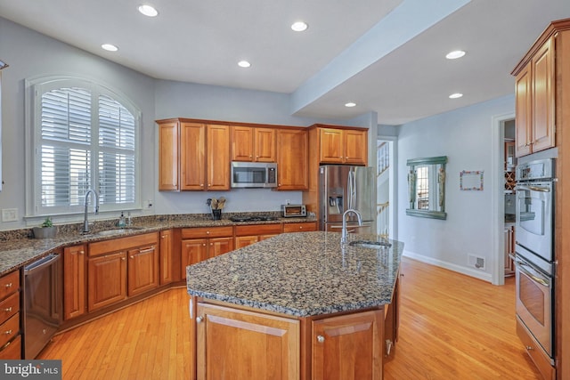 kitchen with stainless steel appliances, sink, a center island with sink, and dark stone counters