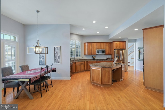 kitchen featuring light hardwood / wood-style flooring, dark stone countertops, an island with sink, pendant lighting, and stainless steel appliances