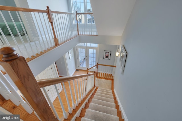 stairs with french doors, a towering ceiling, and hardwood / wood-style flooring