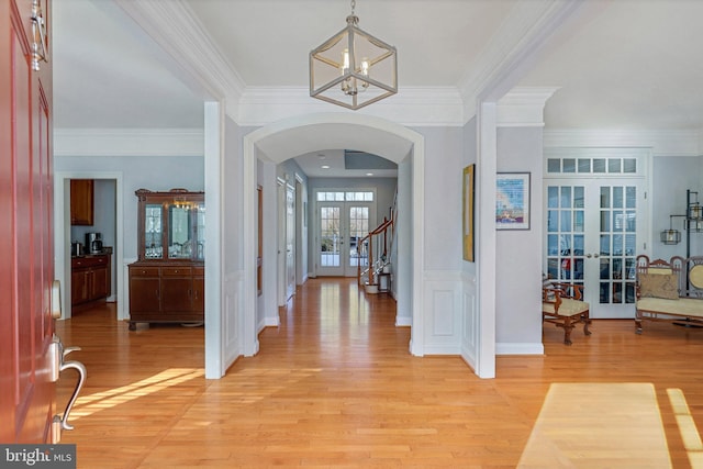 foyer entrance featuring ornamental molding, a chandelier, light hardwood / wood-style floors, and french doors