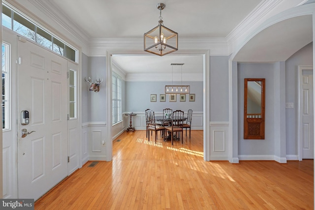 entrance foyer with ornamental molding, light hardwood / wood-style floors, and a notable chandelier