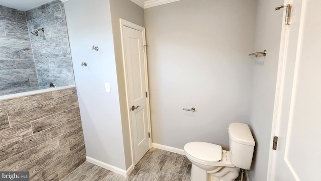 bathroom with ornamental molding, toilet, and a tile shower