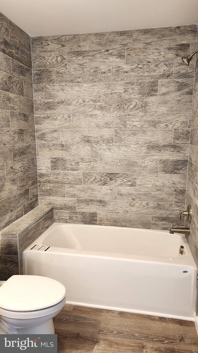 bathroom featuring hardwood / wood-style floors, washtub / shower combination, and toilet