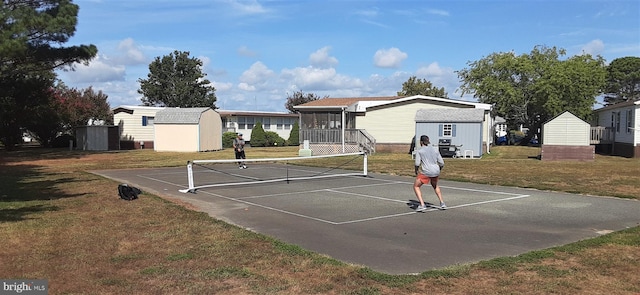 view of tennis court with a yard and a shed