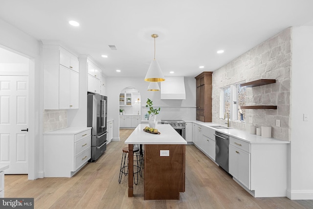 kitchen with wall chimney exhaust hood, high end appliances, a kitchen island, pendant lighting, and white cabinets