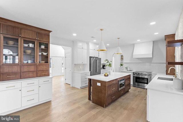 kitchen with pendant lighting, sink, high end appliances, a center island, and wall chimney exhaust hood