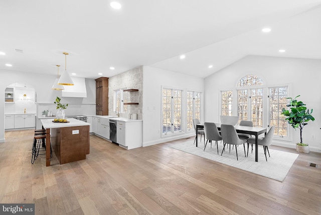 kitchen with white cabinetry, a kitchen island, a kitchen bar, decorative light fixtures, and stainless steel dishwasher