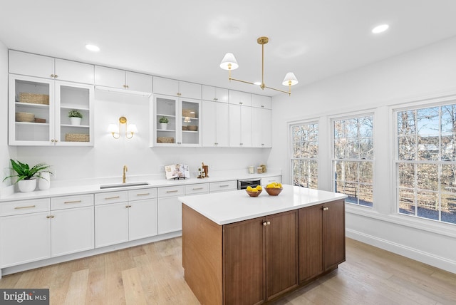 kitchen with white cabinetry, sink, light wood-type flooring, and decorative light fixtures