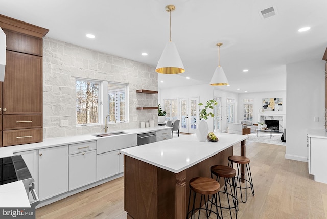 kitchen featuring sink, white cabinetry, hanging light fixtures, light wood-type flooring, and a kitchen island