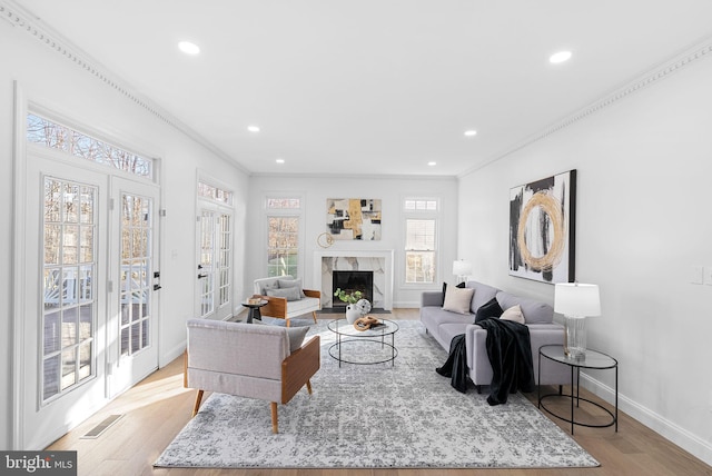 living room featuring crown molding, light hardwood / wood-style flooring, a high end fireplace, and french doors