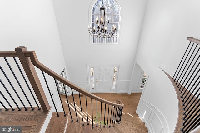 stairway featuring hardwood / wood-style flooring, a towering ceiling, and an inviting chandelier