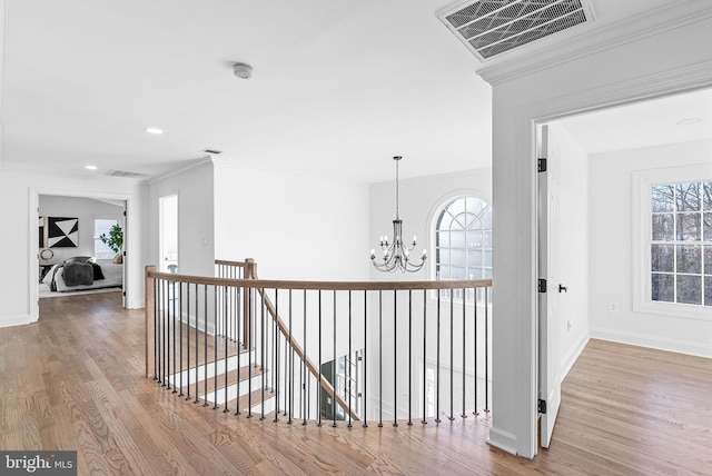 hallway with an inviting chandelier, wood-type flooring, and crown molding