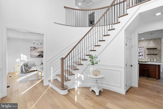 stairs featuring wood-type flooring, a towering ceiling, an inviting chandelier, and crown molding