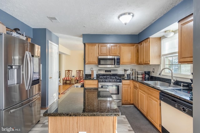 kitchen with a textured ceiling, dark stone counters, sink, a kitchen island, and stainless steel appliances