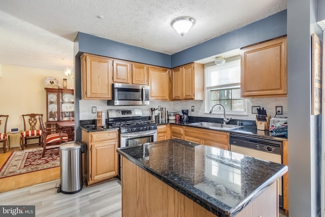 kitchen with light hardwood / wood-style flooring, appliances with stainless steel finishes, sink, a textured ceiling, and a kitchen island