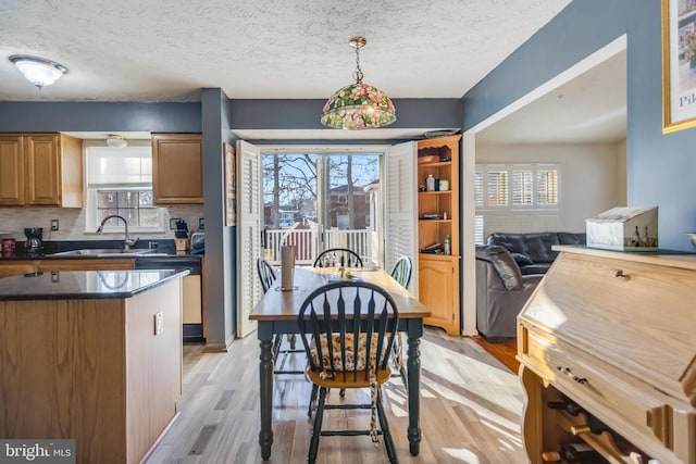 kitchen with a textured ceiling, a center island, sink, hanging light fixtures, and light hardwood / wood-style flooring