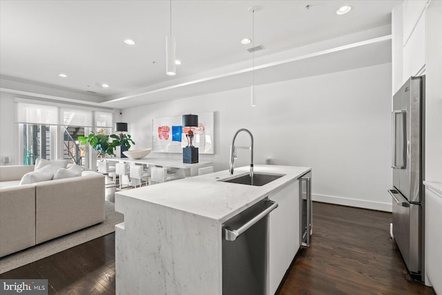 kitchen featuring a raised ceiling, sink, appliances with stainless steel finishes, white cabinetry, and a center island with sink