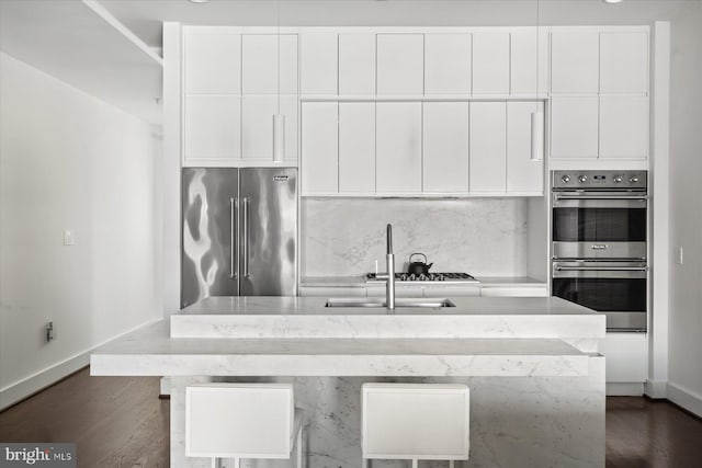 kitchen featuring appliances with stainless steel finishes, sink, backsplash, white cabinetry, and an island with sink