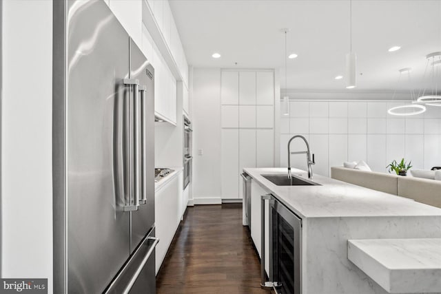 kitchen featuring appliances with stainless steel finishes, sink, decorative light fixtures, light stone countertops, and beverage cooler