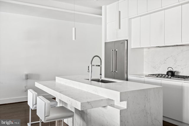 kitchen featuring sink, stainless steel appliances, light stone counters, and a center island with sink