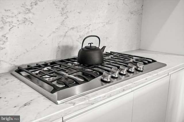 room details with decorative backsplash, white cabinets, and stainless steel gas stovetop