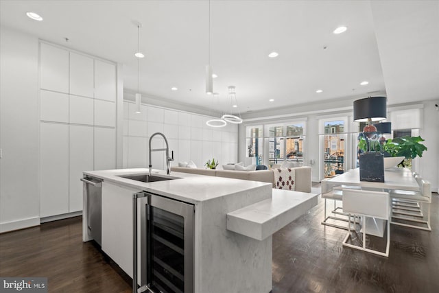 kitchen with sink, decorative light fixtures, white cabinets, a kitchen island with sink, and beverage cooler