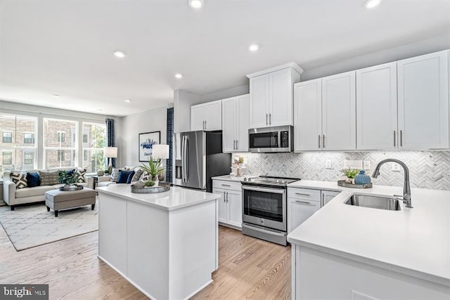 kitchen featuring appliances with stainless steel finishes, sink, white cabinetry, a center island, and light hardwood / wood-style floors