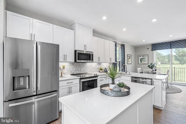 kitchen featuring appliances with stainless steel finishes, a kitchen island, white cabinetry, decorative backsplash, and kitchen peninsula