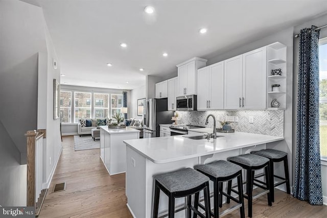 kitchen with appliances with stainless steel finishes, white cabinets, sink, kitchen peninsula, and a breakfast bar area