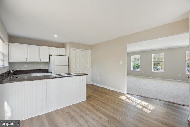 kitchen featuring kitchen peninsula, sink, white cabinetry, dark stone countertops, and white fridge