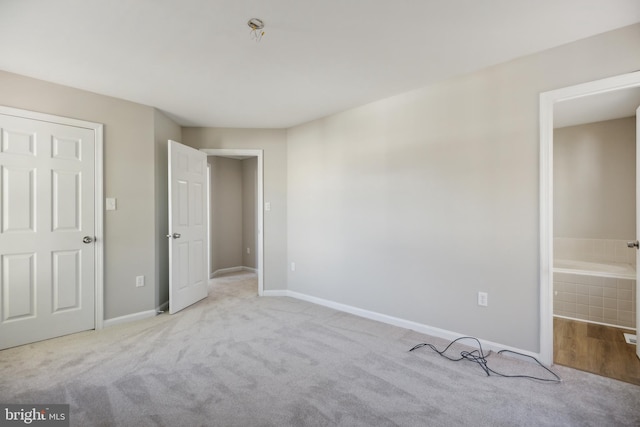 unfurnished bedroom featuring light colored carpet and ensuite bath