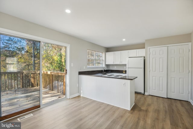 kitchen featuring kitchen peninsula, hardwood / wood-style floors, white cabinetry, and white fridge