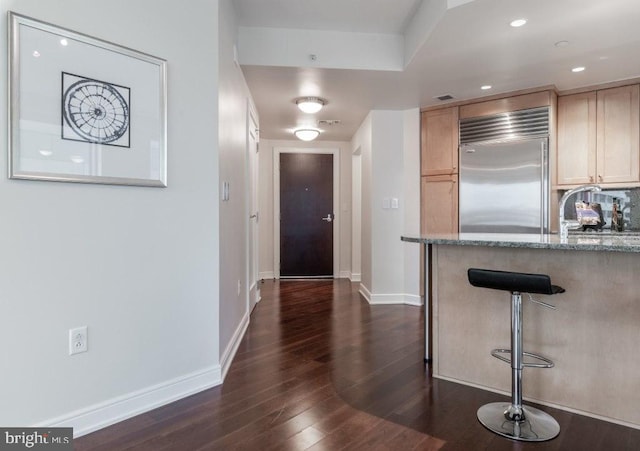 kitchen with sink, dark wood-type flooring, built in refrigerator, stone countertops, and light brown cabinetry