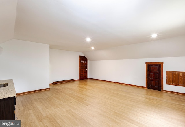 spare room featuring a baseboard radiator, light wood-type flooring, and vaulted ceiling