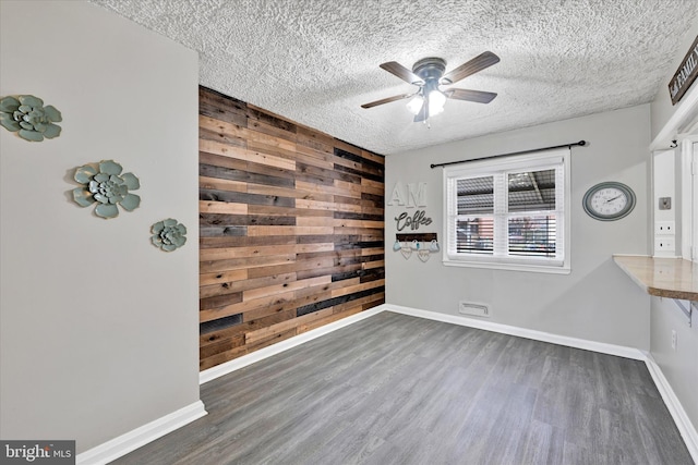 spare room featuring ceiling fan, wooden walls, dark hardwood / wood-style floors, and a textured ceiling