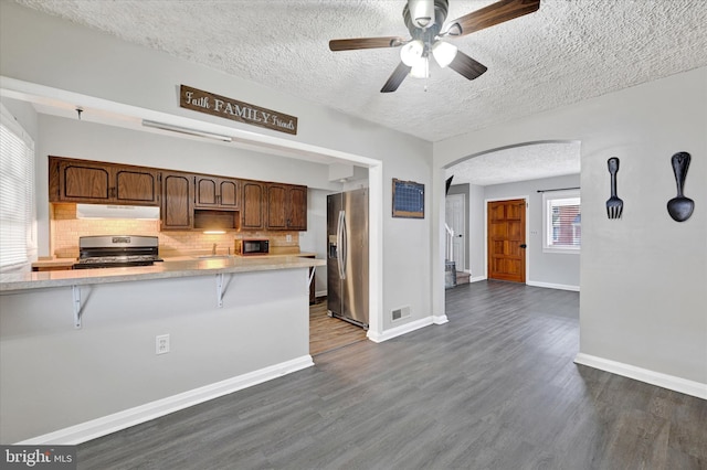 kitchen with dark wood-type flooring, a breakfast bar, stainless steel fridge, kitchen peninsula, and stove