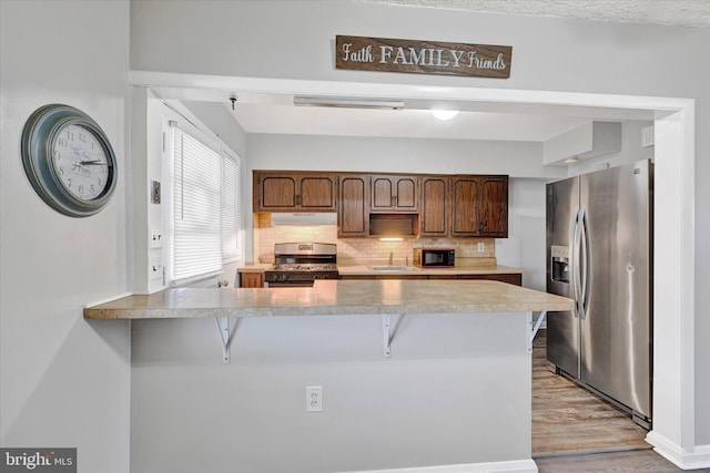 kitchen with appliances with stainless steel finishes, tasteful backsplash, light hardwood / wood-style floors, a kitchen bar, and kitchen peninsula